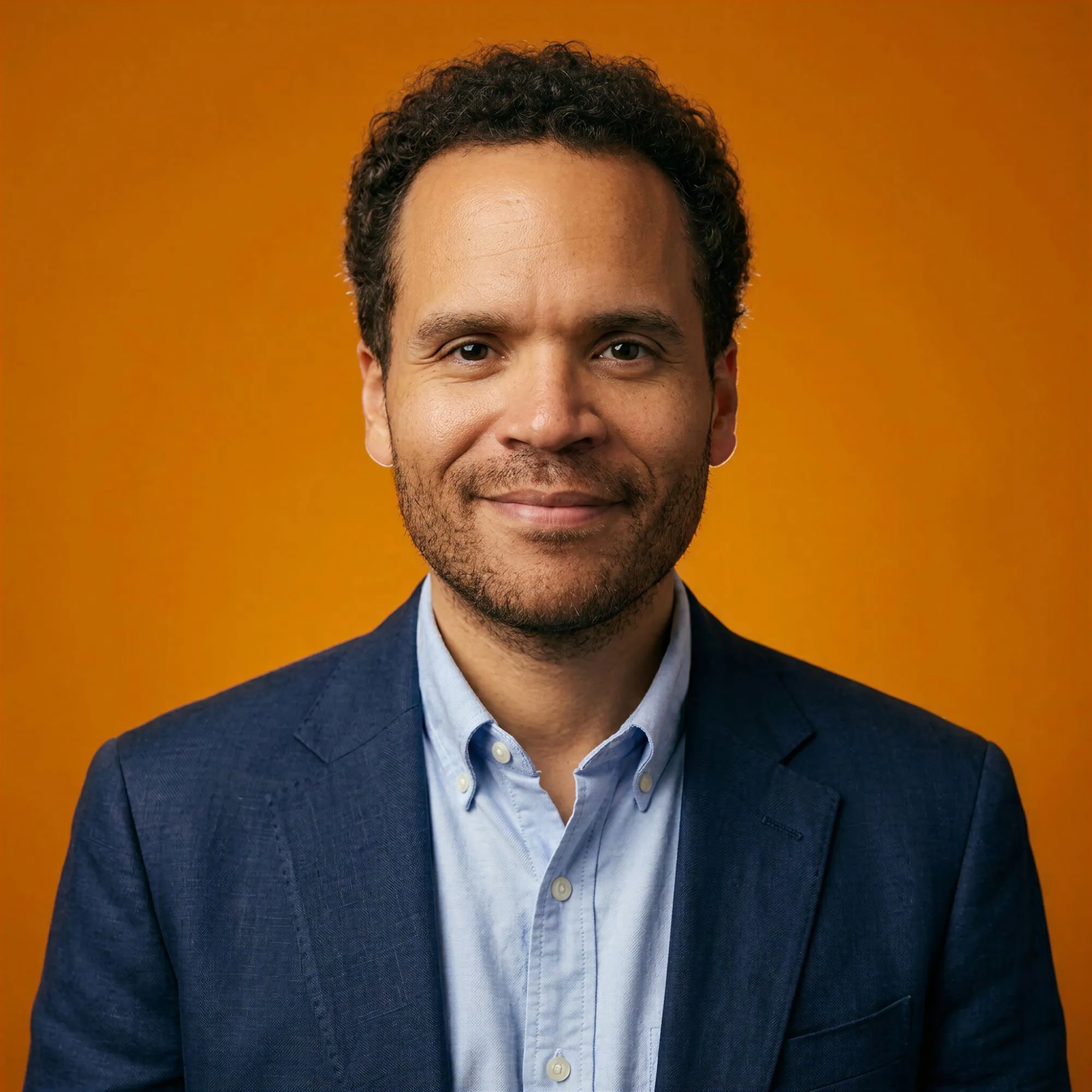Portrait of Ryan J. Smith in a navy blazer against an amber backdrop