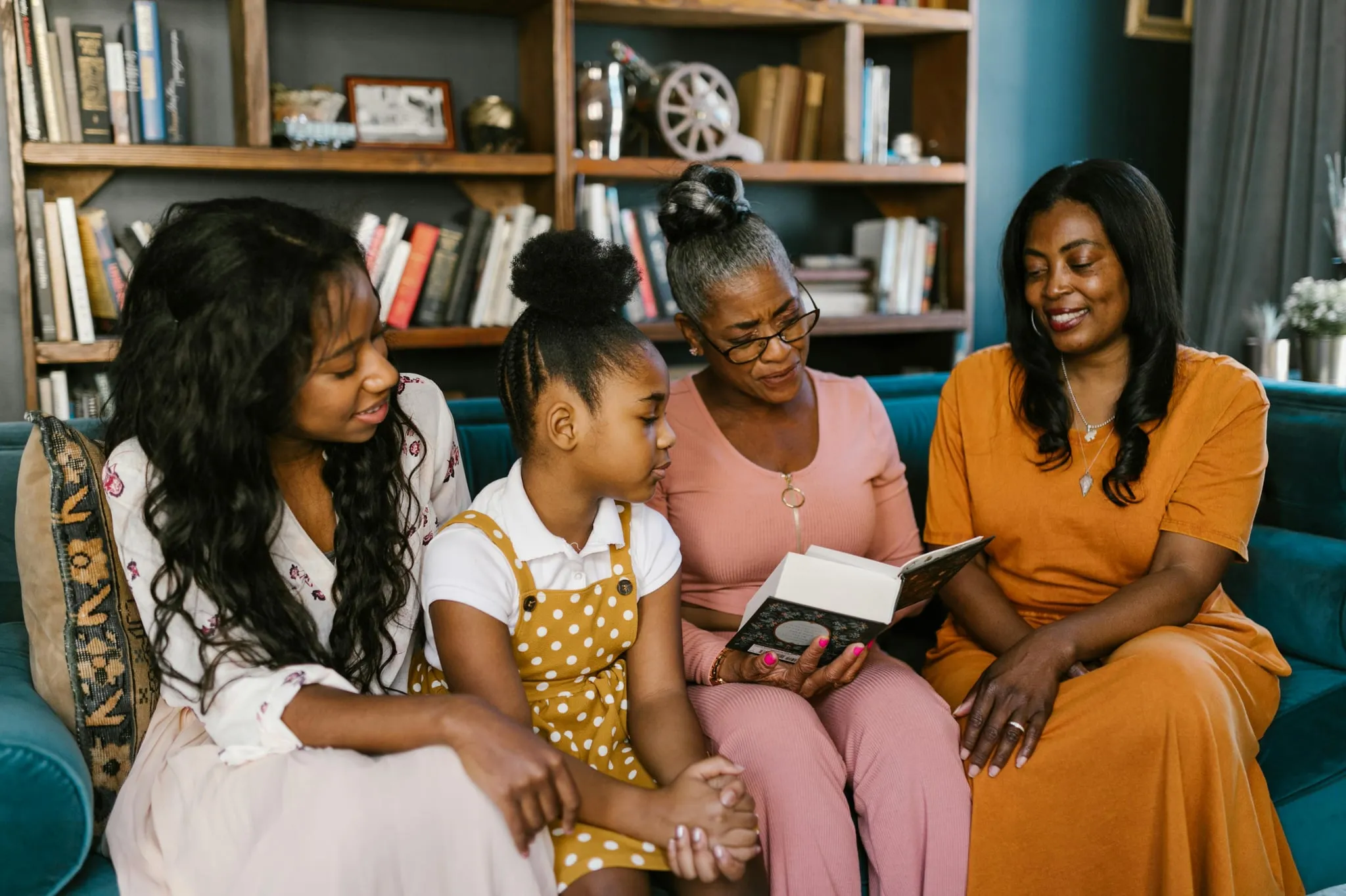 Three generations of women on a couch, the grandmother reading aloud from an open book
