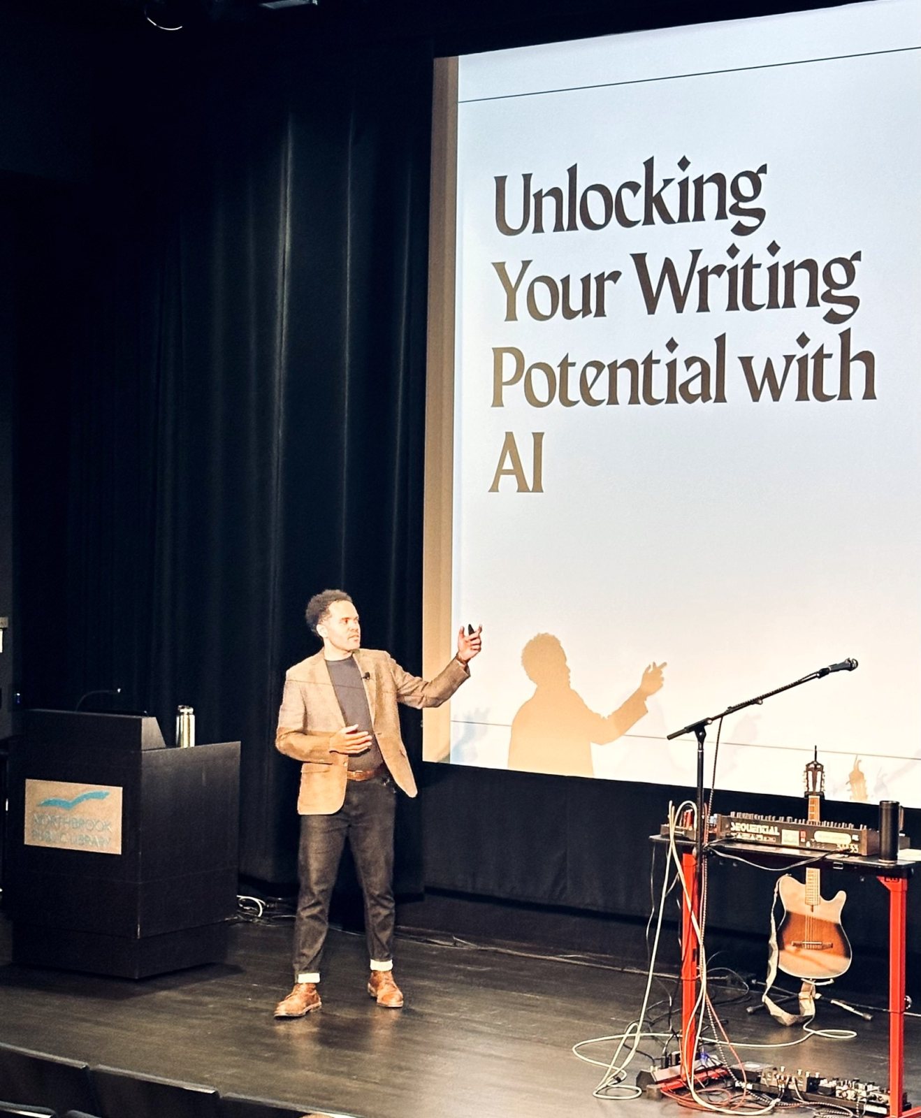 Ryan J. Smith on stage at Northbrook Public Library, gesturing toward a slide that reads Unlocking Your Writing Potential with AI